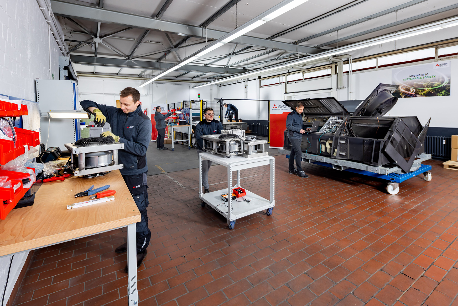 Mitsubishi Electric Workshop technicians working on transportation system parts.